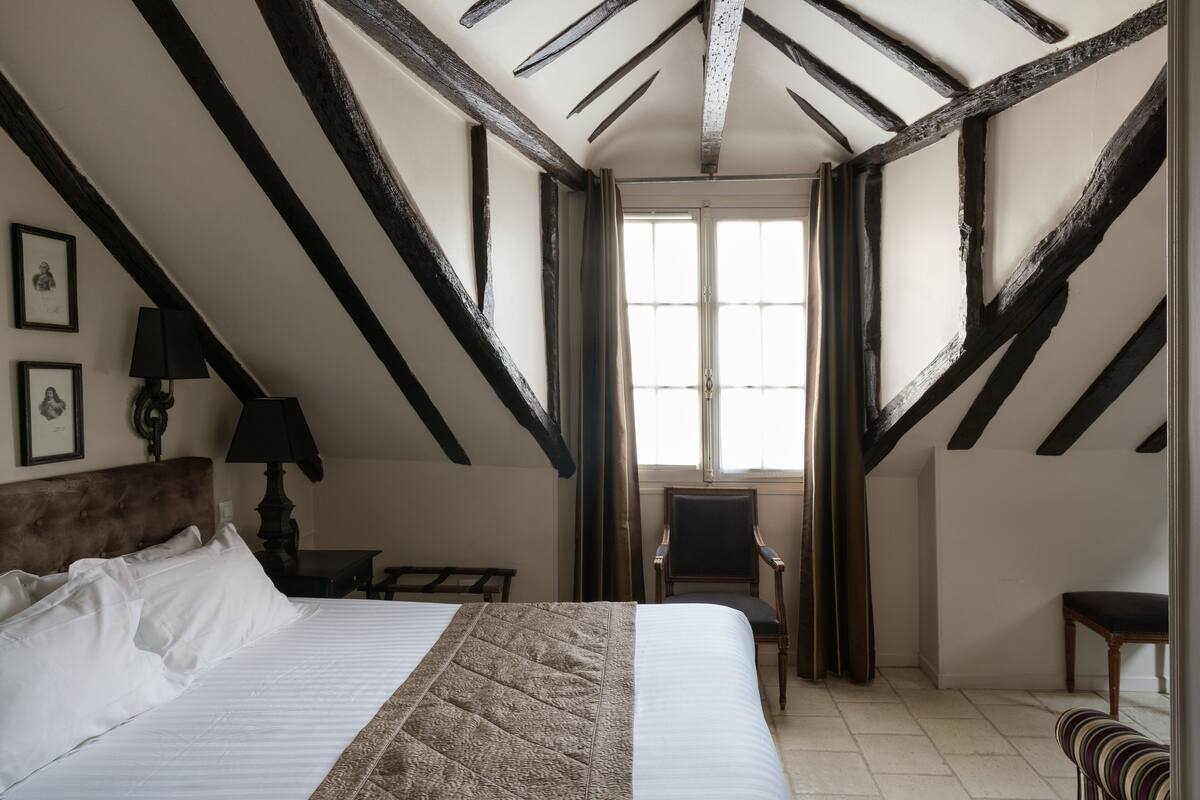 A bedroom with a large bed, a chair, a desk, and a window with curtains.