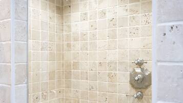 A small, tiled shower with a handheld showerhead and a control knob.