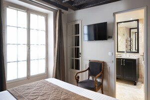 Un dormitorio con cama, una silla, un televisor y un baño con lavamanos y espejo.