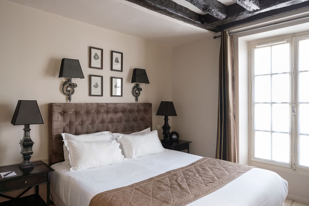 A hotel room with a large bed, two bedside tables with lamps, a headboard, and a window with curtains.