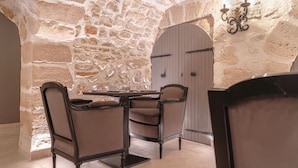 A stone-walled dining area with a table and chairs, a door with a decorative handle, and a wall-mounted light fixture. - Hôtel Saint-Louis Marais (Paris)