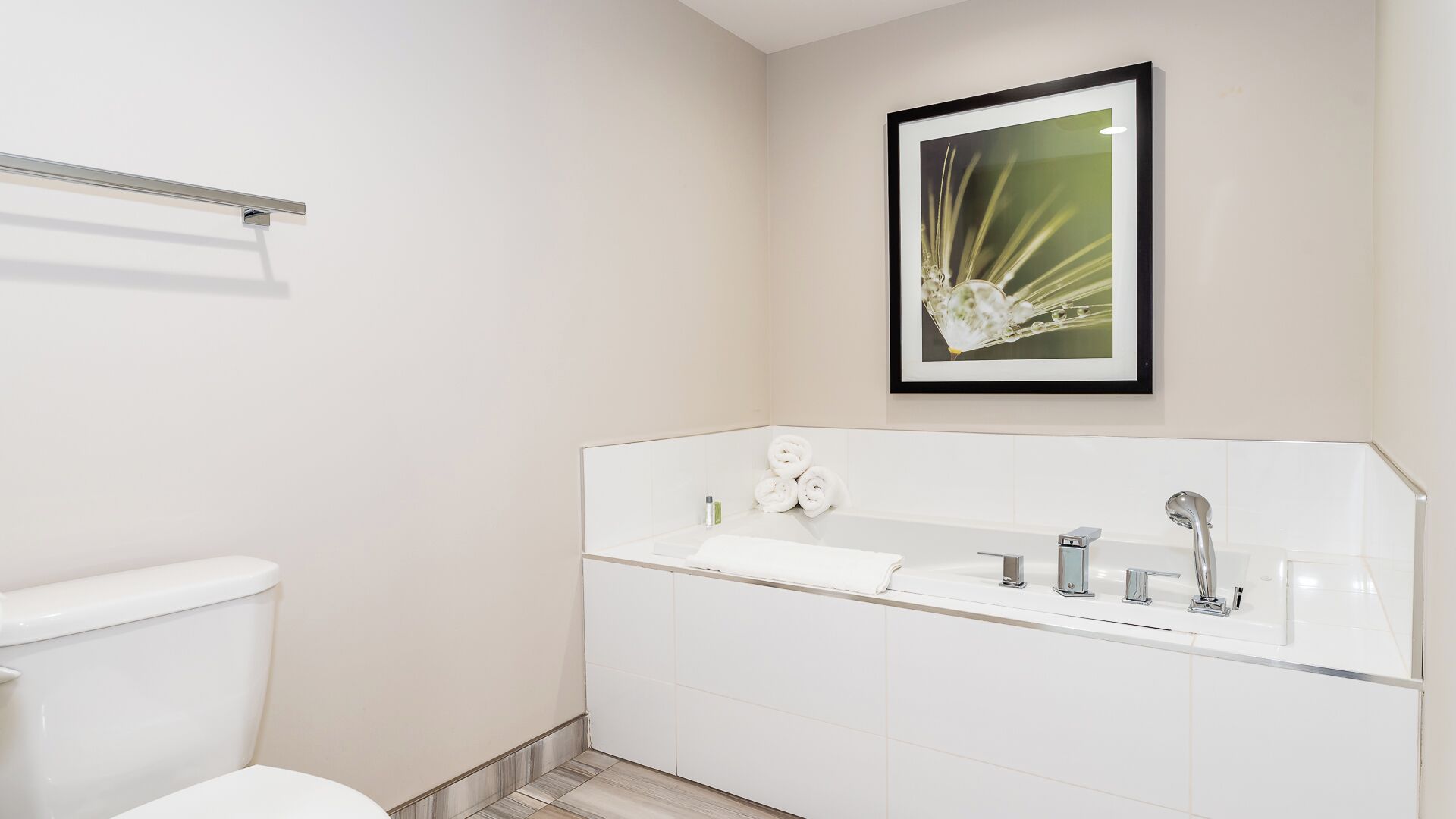 Un baño moderno con lavamanos con estructura de vidrio, un inodoro y un cuadro enmarcado en la pared.