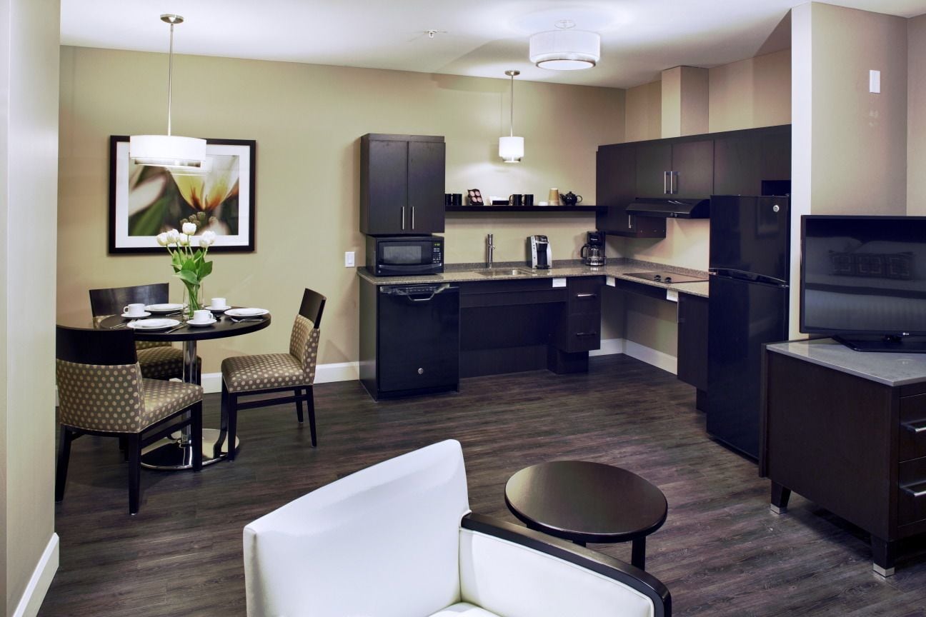 A modern kitchen with dark cabinetry, a dining area with a round table and chairs, and a television on a stand.
