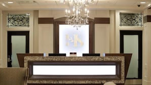 Un hall d’hôtel avec un comptoir de réception en marbre, un lustre et deux portes dotées de panneaux en verre dépoli.