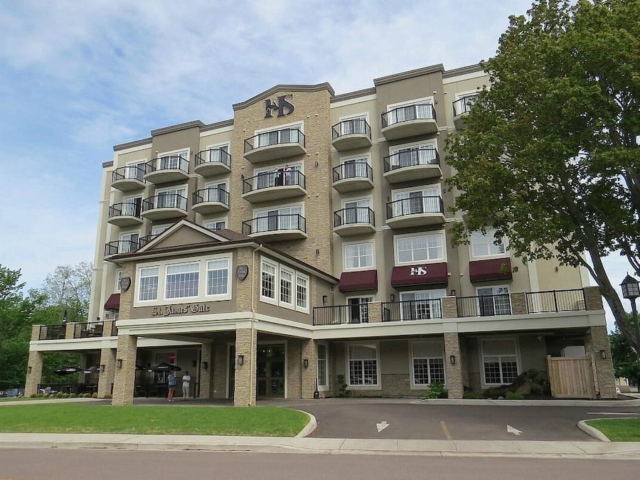 A multi-story hotel with a central entrance, balconies on each floor, and a landscaped front yard.