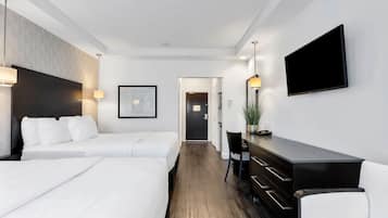 A hotel room with two beds, a desk, a chair, a TV, and a door leading to another room.