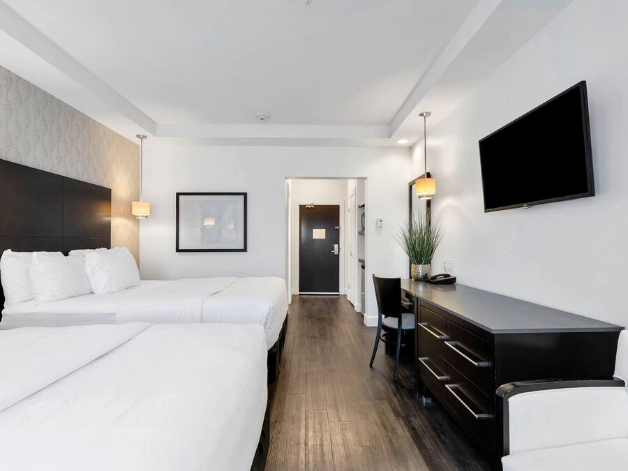 A hotel room with two beds, a desk, a chair, a TV, and a door leading to another room.