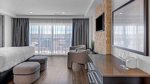 Une chambre d’hôtel moderne dotée d’un grand lit, d’un coin salon avec des poufs, d’un téléviseur fixé à un mur en briques et offrant une vue sur la ville grâce à de grandes fenêtres.