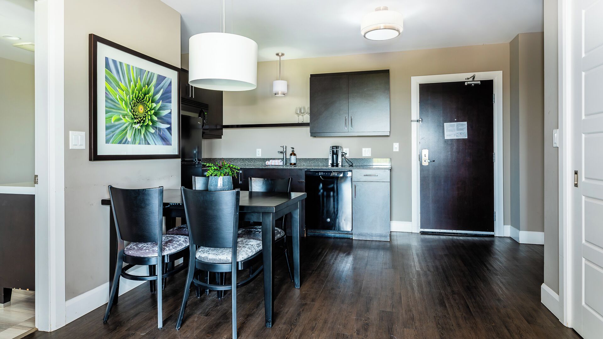 A modern kitchen with dark cabinets, a dining area with a table and chairs, and a large framed picture on the wall.