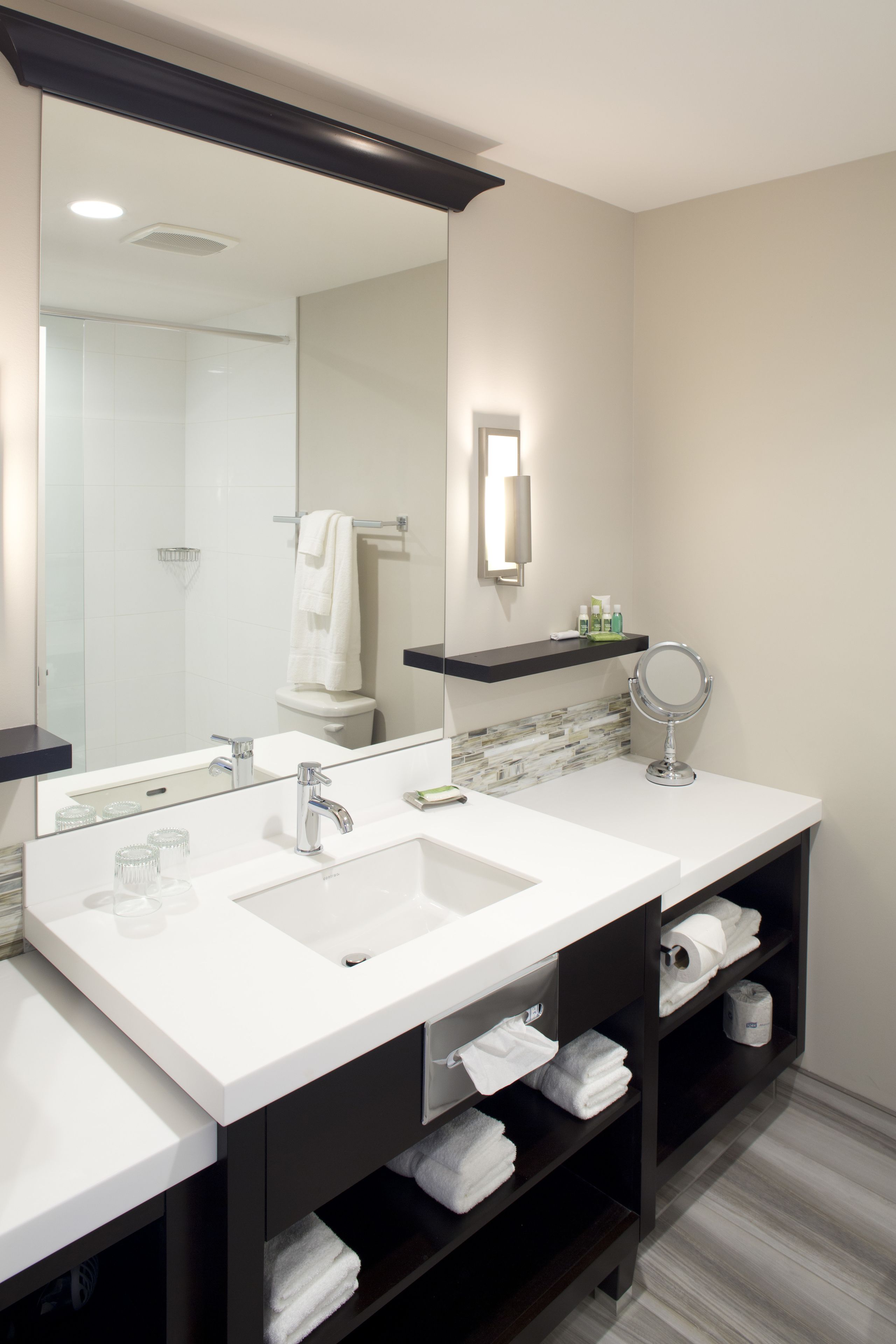 A modern bathroom with two sinks, a large mirror, and a towel rack.