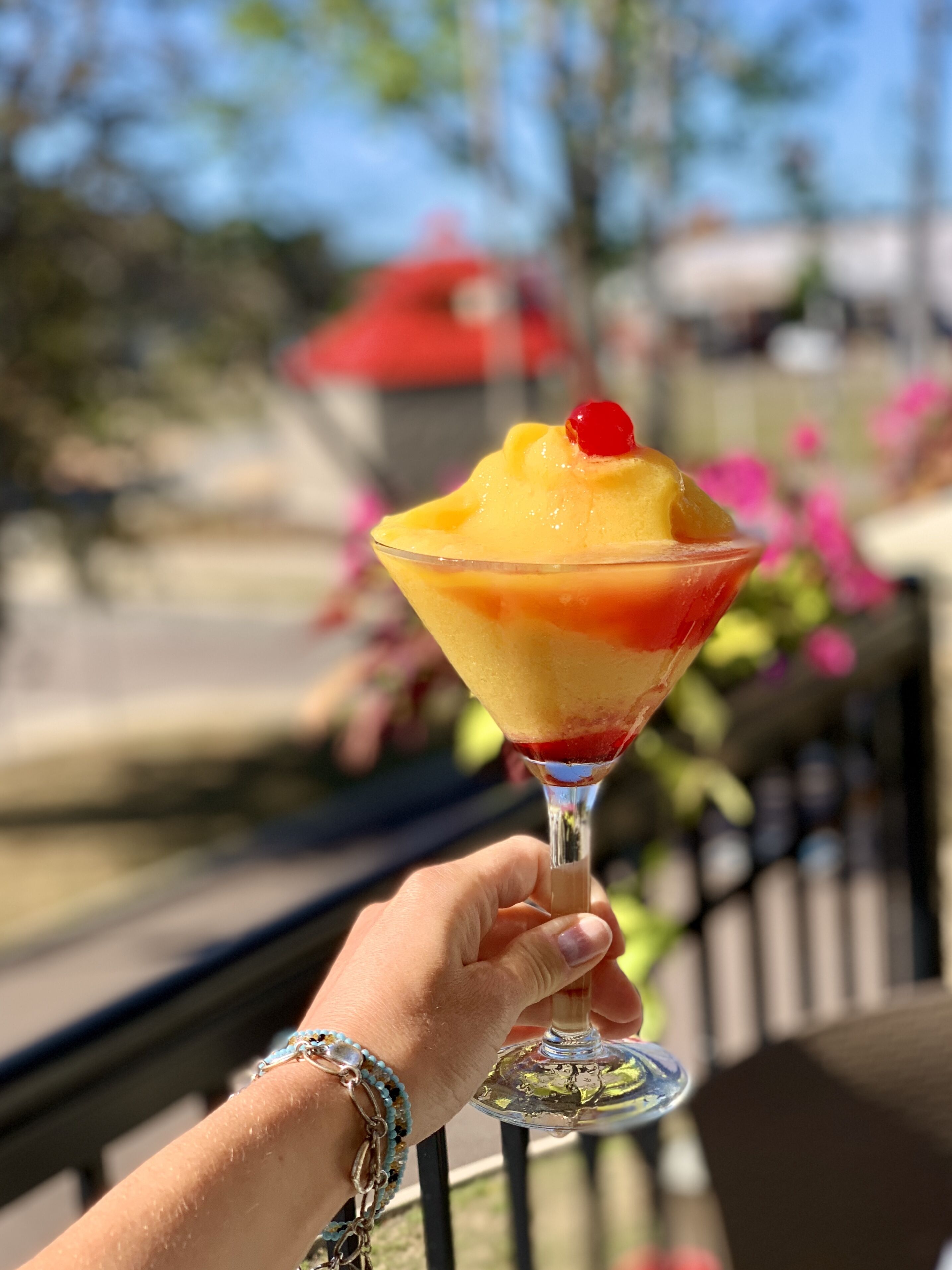 A hand holding a cocktail glass with a layered drink and a cherry on top.
