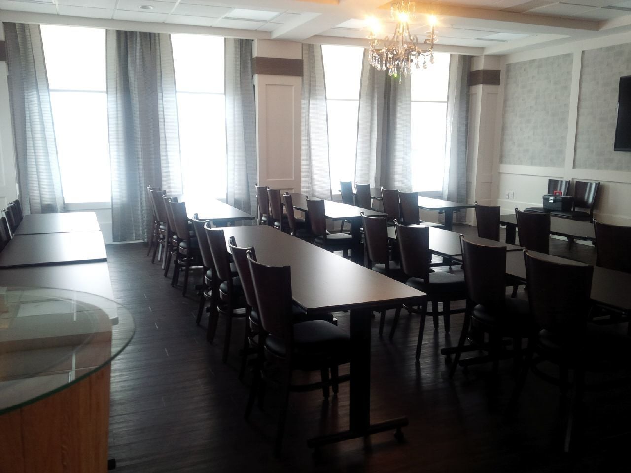 A conference room with multiple tables and chairs, large windows with curtains, and a chandelier.