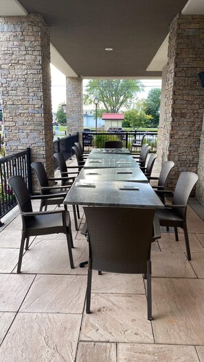 Une terrasse extérieure avec une longue table et des chaises, des piliers en pierre et une vue sur les environs.
