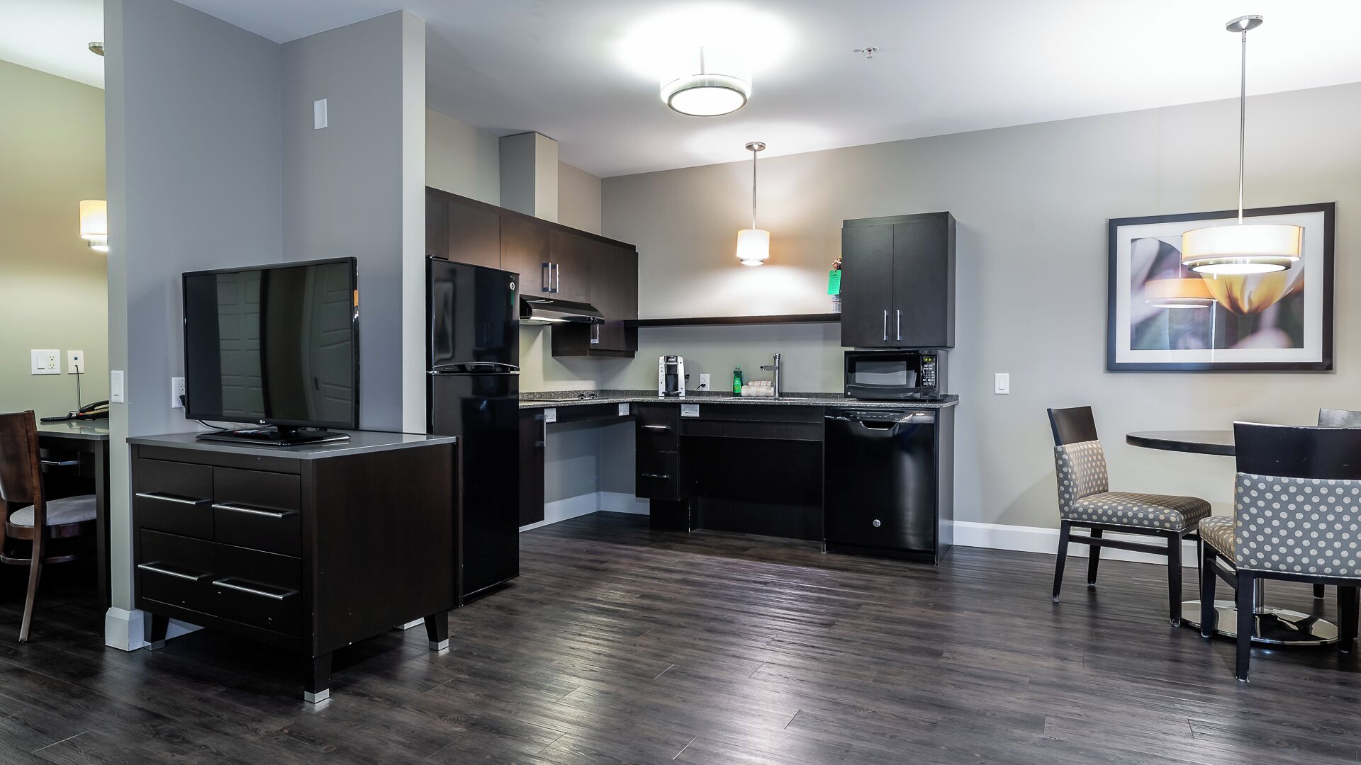 A modern kitchen with dark cabinetry, a built-in oven, and a dining area with a small table and two chairs.
