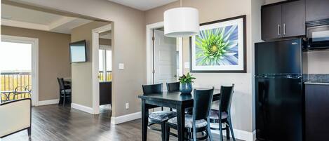 A modern kitchen with dark cabinetry, a black refrigerator, and a dining area with a table and chairs.