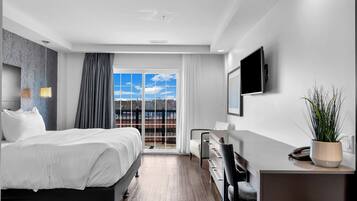 A modern hotel room with a large bed, a desk, a chair, a TV, and a view of the outdoors.