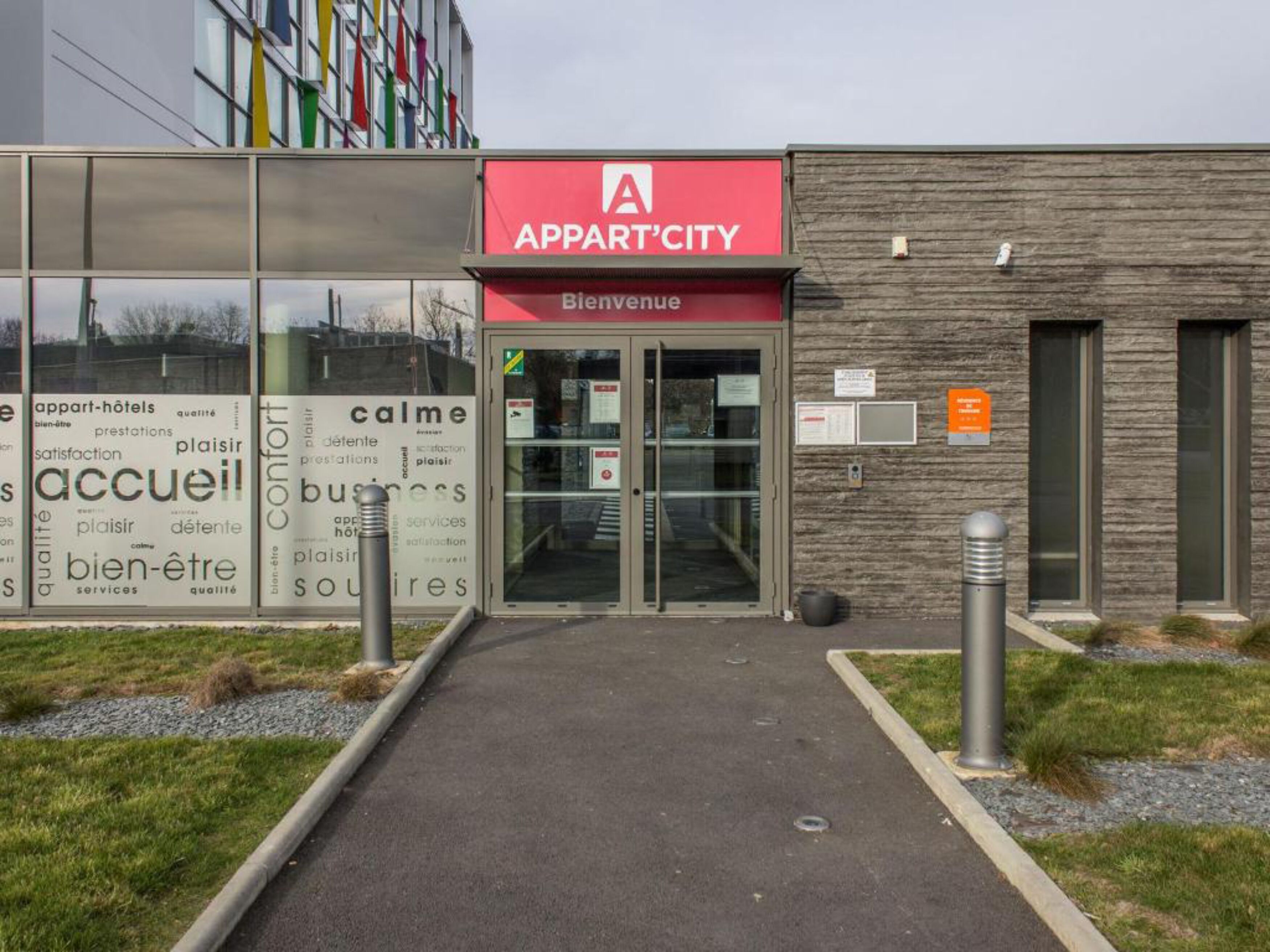 A modern building with a red sign reading "APPART'CITY" and a welcome sign.
