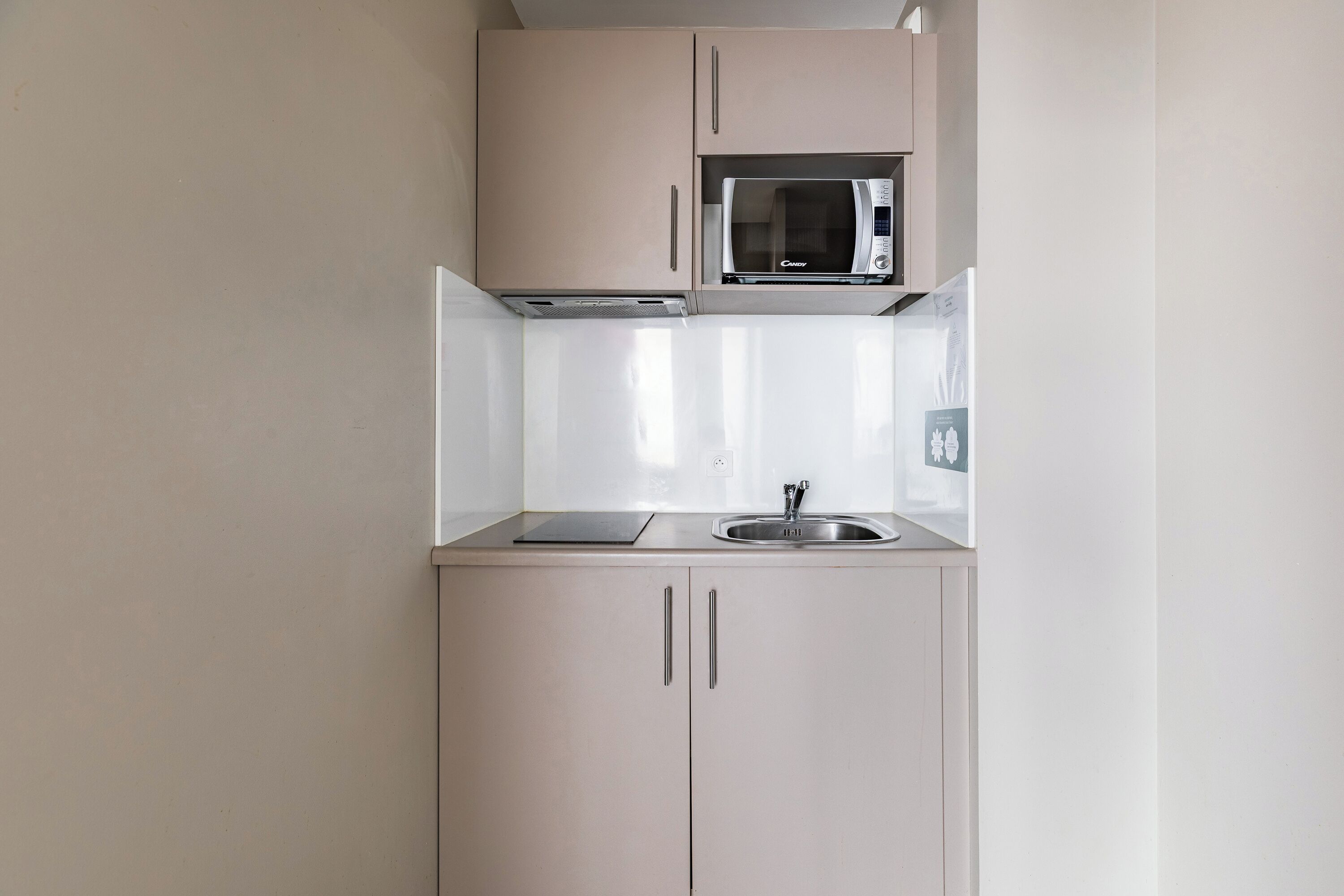 A kitchenette with a microwave, sink, and two cabinets.