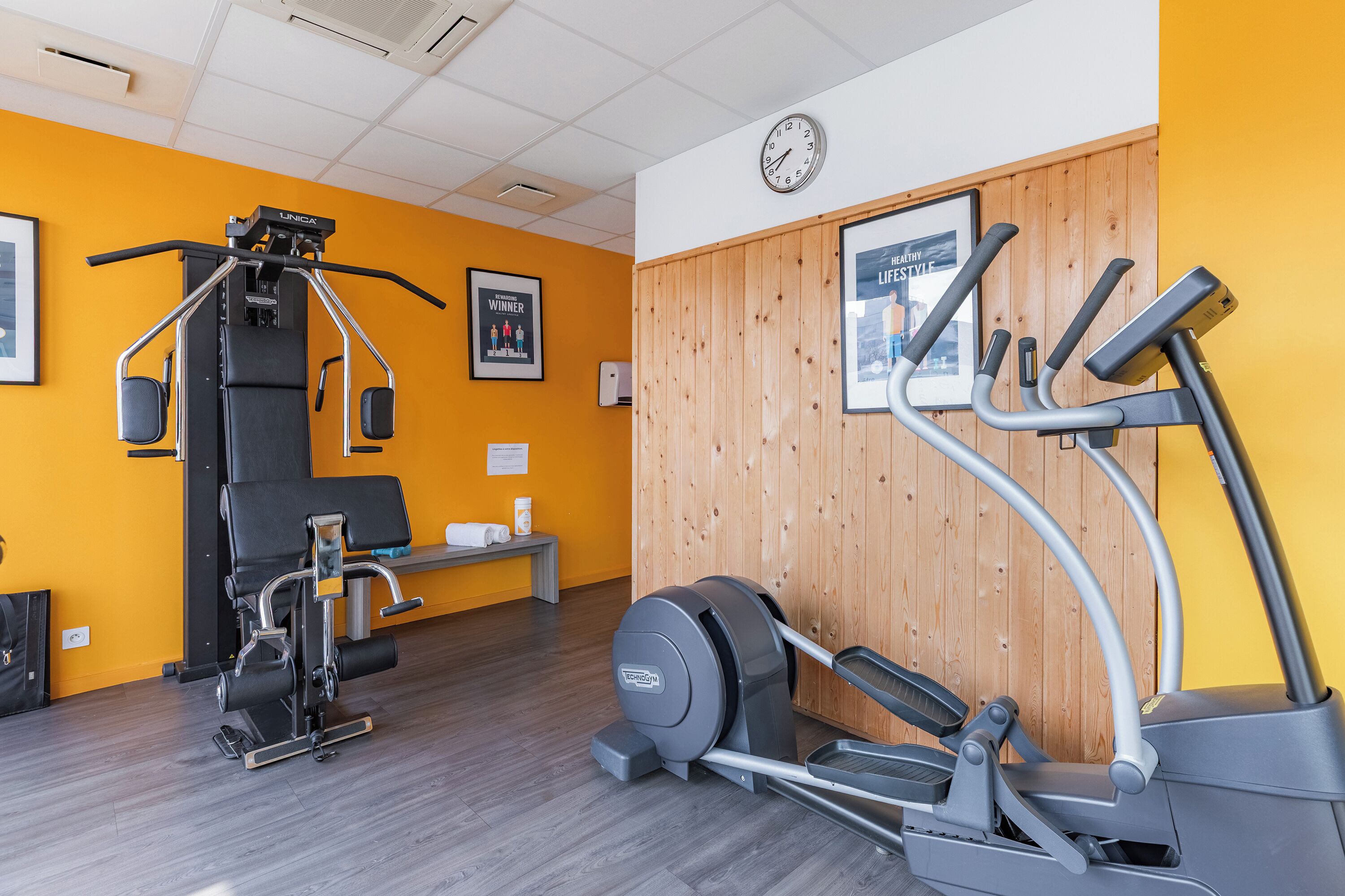 A gym with exercise equipment, a clock, and motivational posters on the wall.