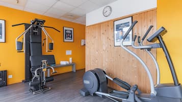 Un gimnasio con equipo de ejercicio, un reloj y carteles motivacionales en la pared.
