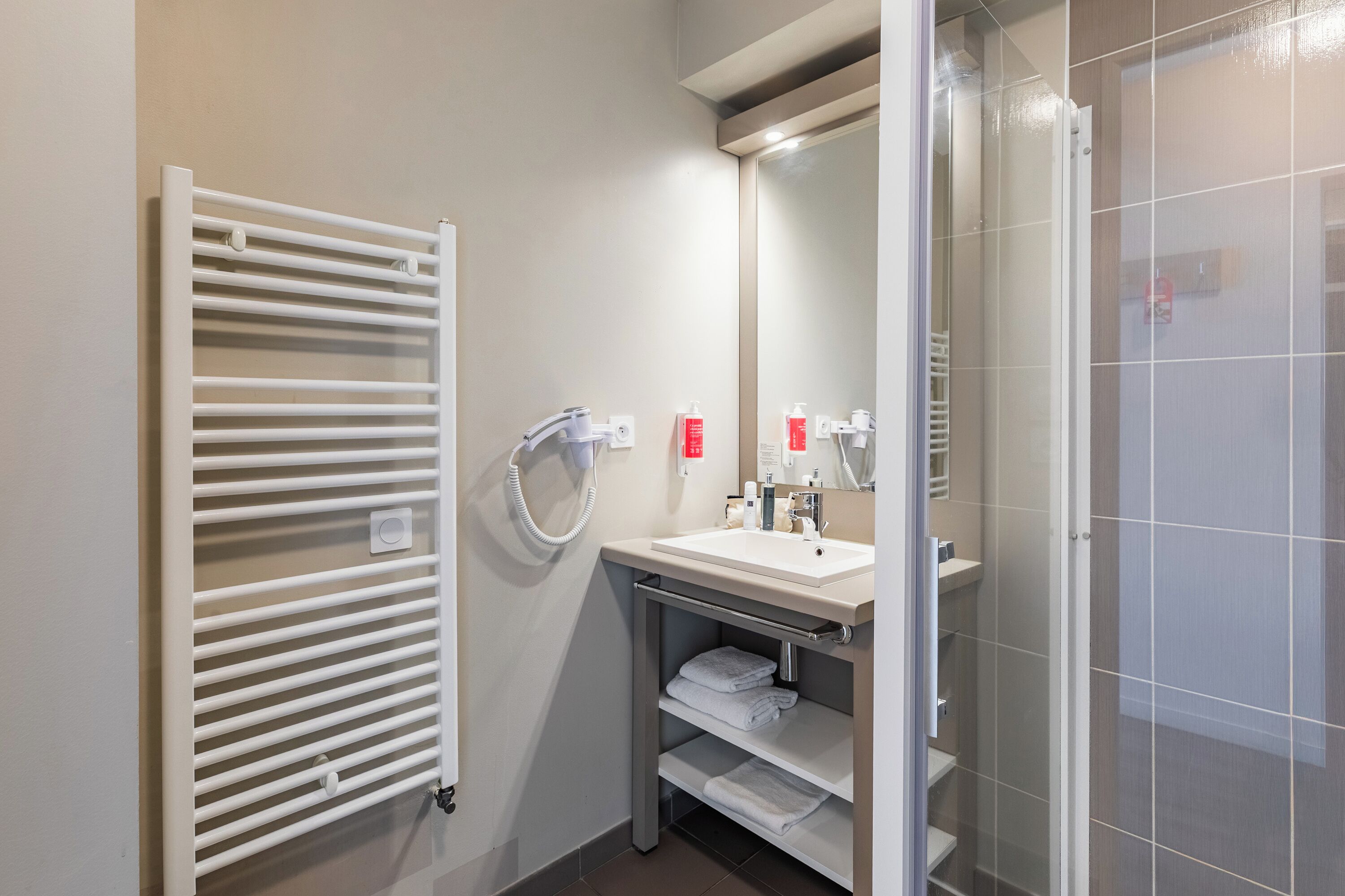 A modern bathroom with a white radiator, a sink with a mirror, and a glass shower enclosure.