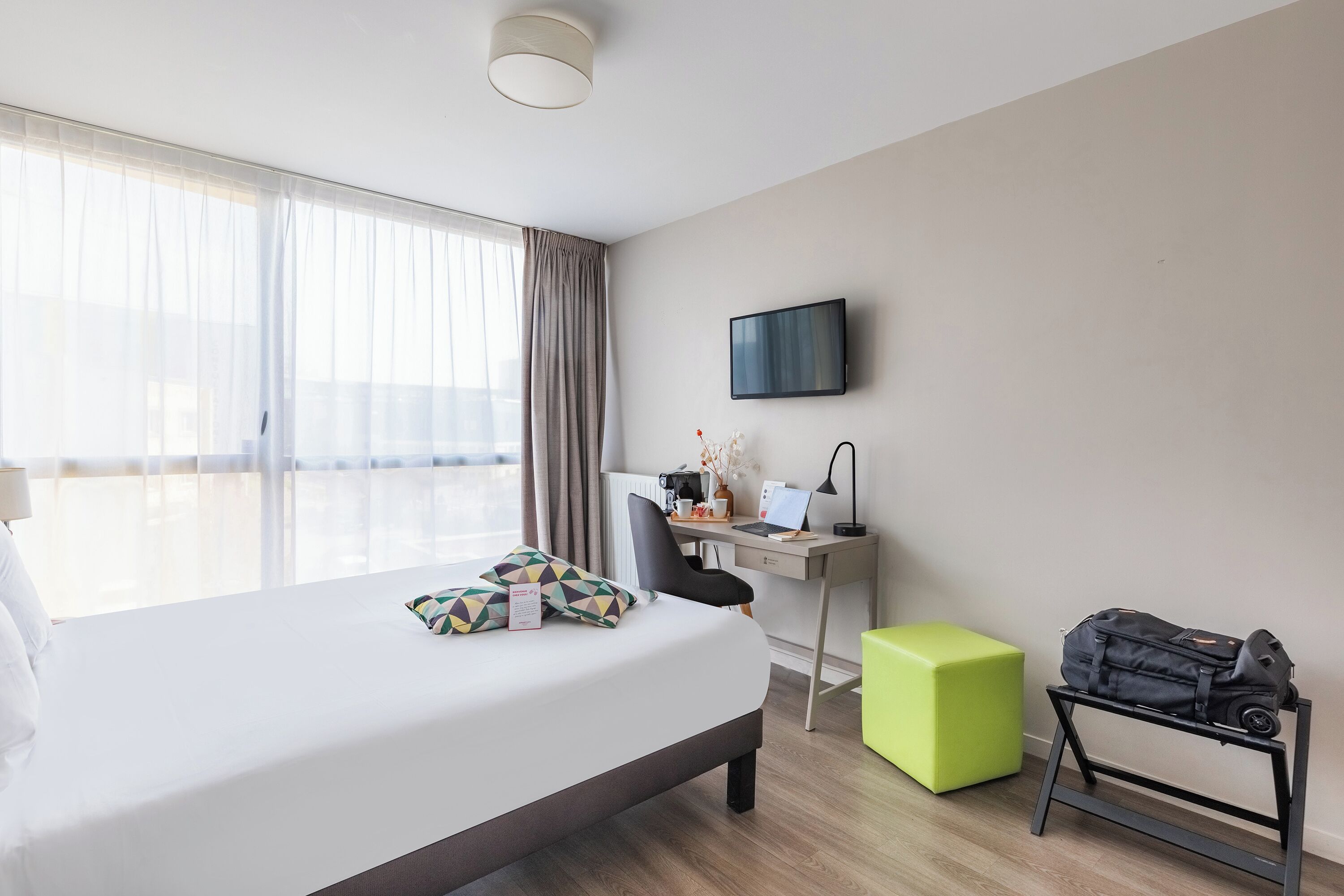 A hotel room with a bed, a desk, a chair, a TV, and a luggage rack.