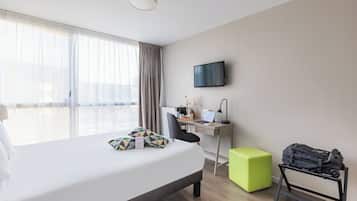 Ein Hotelzimmer mit Bett, Schreibtisch, Stuhl, Fernseher und Gepäckträger.