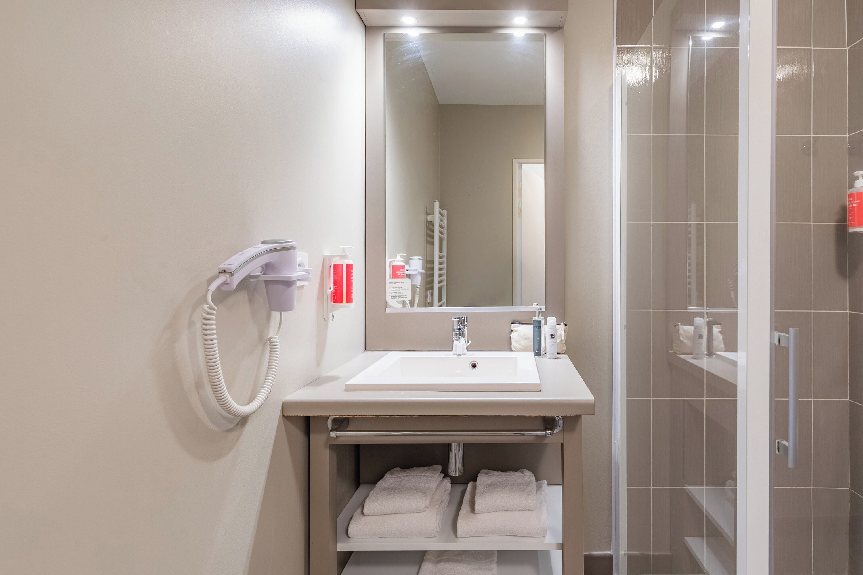 Un baño moderno con lavamanos blanco, espejo y cabina de ducha de vidrio.