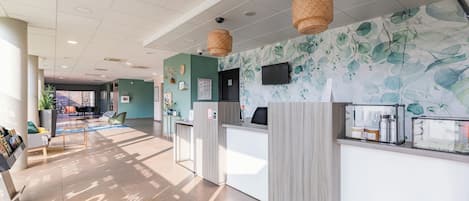 Zona de recepción con mostrador, televisión y pared con diseño de hojas.