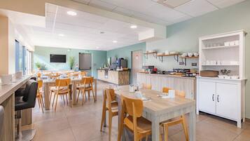 Un espace repas moderne, doté de plusieurs tables et chaises, d’un comptoir de cuisine et d’un téléviseur fixé au mur.