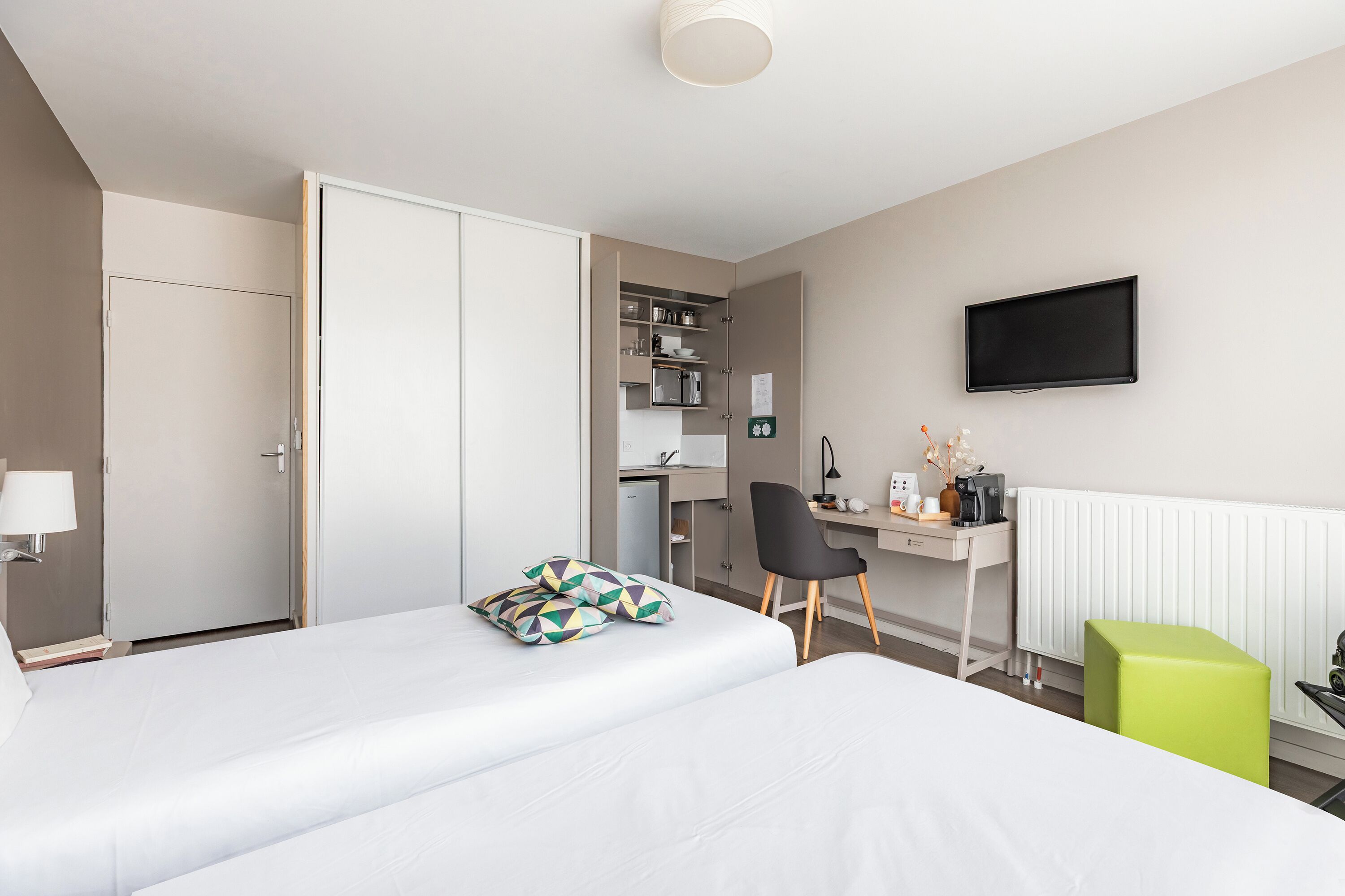 Une chambre d’hôtel avec deux lits, un bureau, une chaise, une télévision et une kitchenette.