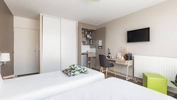 Habitación de hotel con dos camas, un escritorio, una silla, un televisor y una kitchenette.