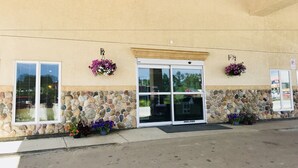 A building with a stone facade, a large glass entrance, and flower planters on the ground level. - Big Lake Inn (Slave Lake)