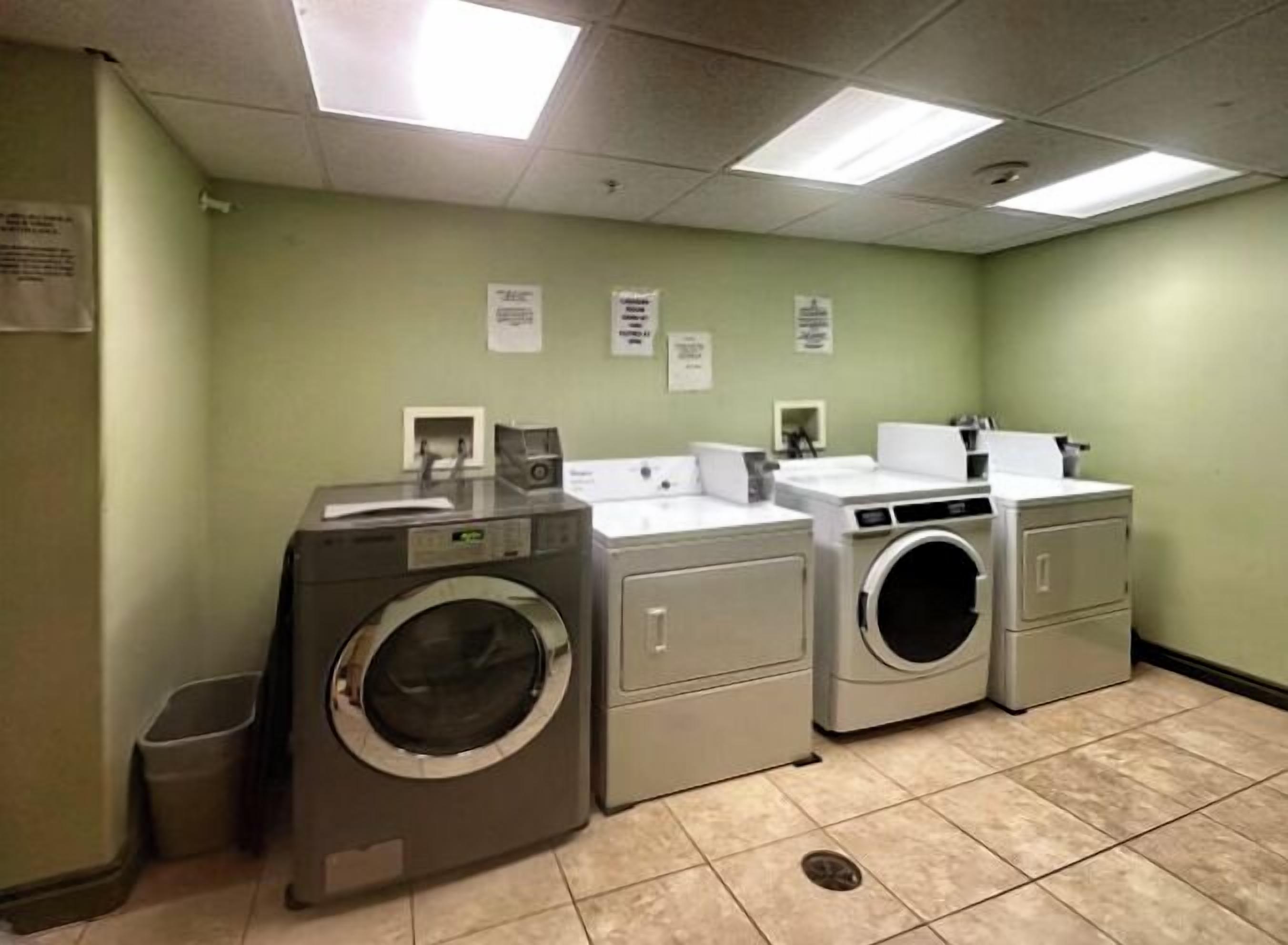A laundry room with two front-loading washing machines, a dryer, and a sink.