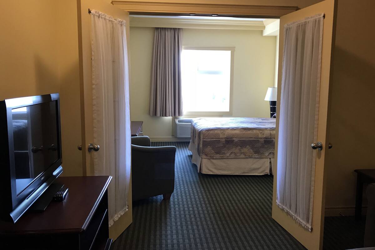 A hotel room with a bed, a desk with a TV, a chair, and a window with curtains.