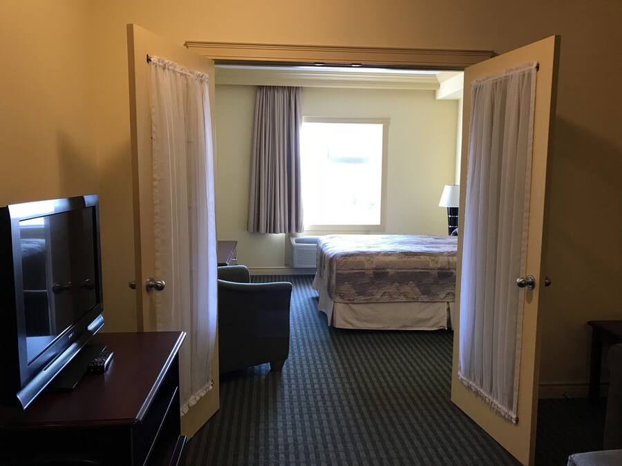 A hotel room with a bed, a desk with a TV, a chair, and a window with curtains.