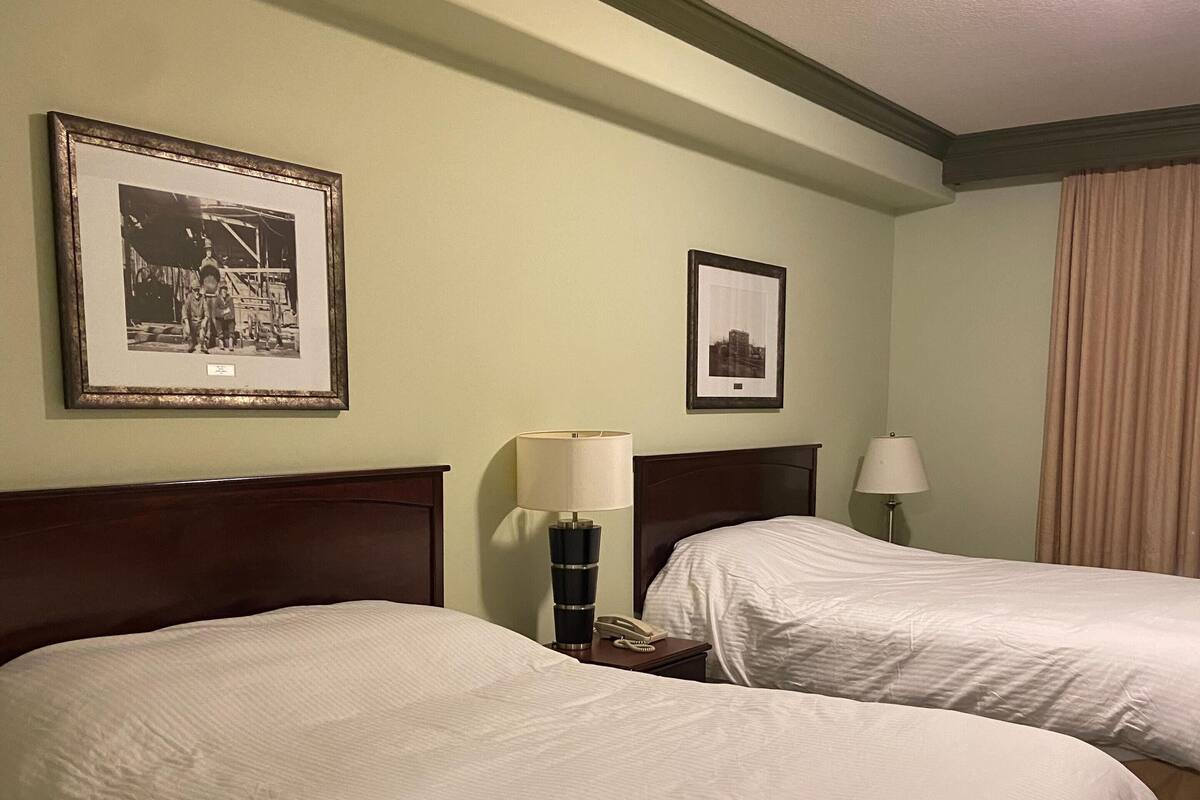 A hotel room with two beds, a nightstand with a lamp, and framed pictures on the wall.