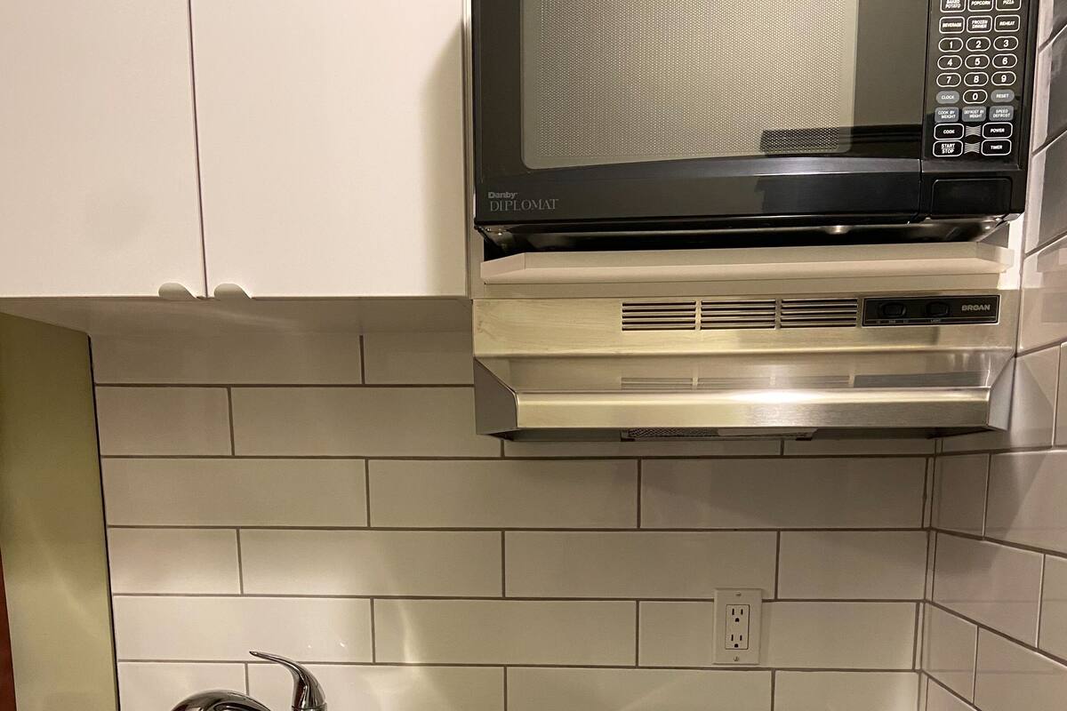 A kitchen with a stainless steel sink, a black countertop, a built-in microwave, and white cabinets.