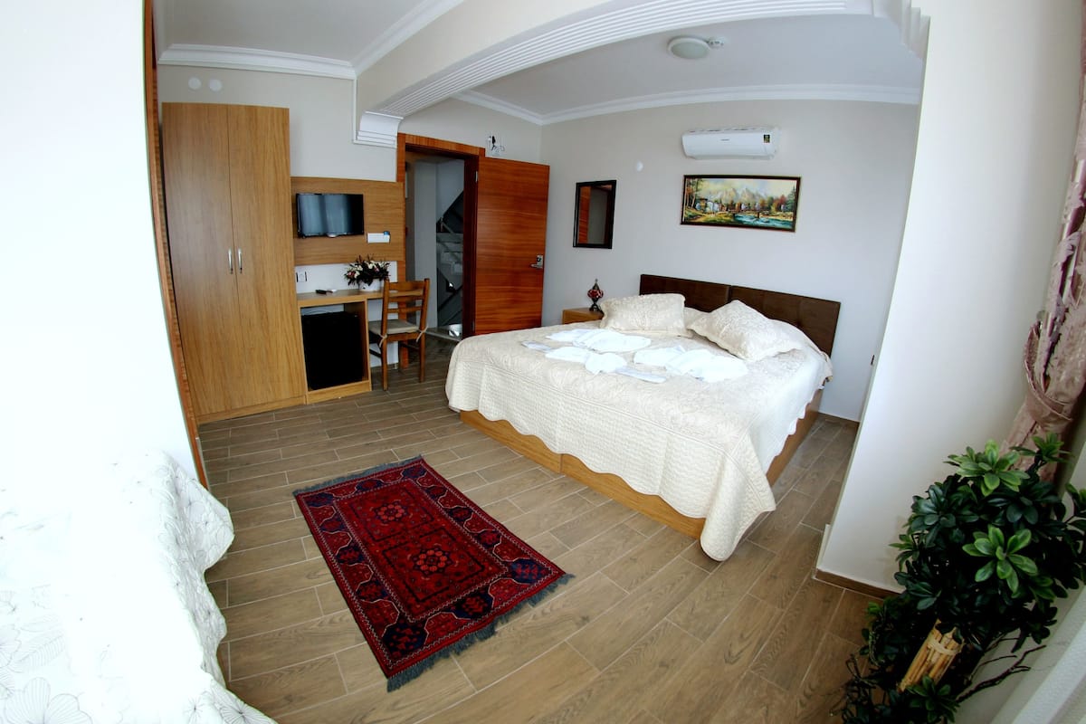 A bedroom with a bed, a desk, a chair, a red rug, and a staircase.