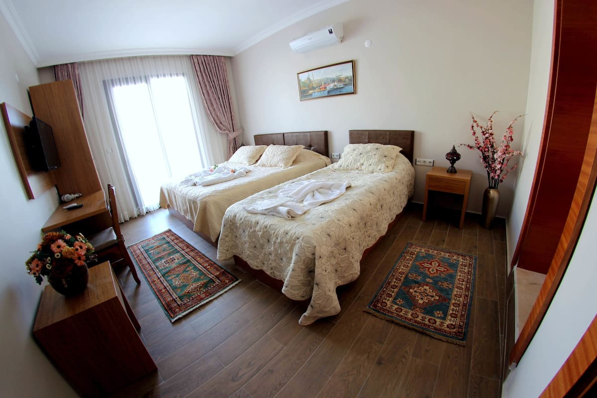 A hotel room with two beds, a desk, a chair, a TV, and a window with curtains.