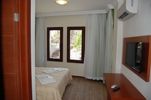 A hotel room with a bed, a TV, a wooden desk, and two windows with curtains.