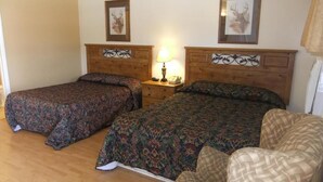 Una habitación con dos camas, una silla y una mesita de noche con lámpara.