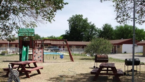 Un parque infantil con tobogán y columpios, mesas de picnic y una parrilla.