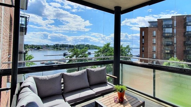 Un balcon avec un canapé et un pot de fleurs, donnant sur une rivière et des immeubles.