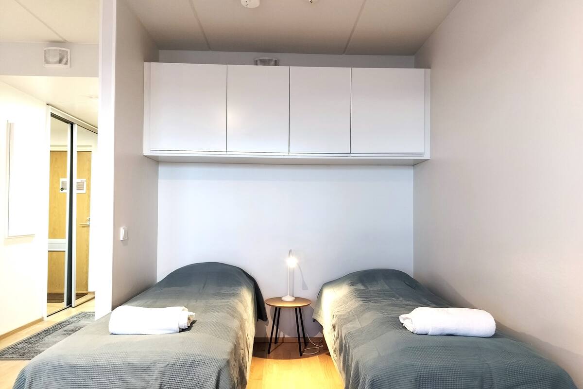 Une chambre avec deux lits simples, une petite table avec une lampe et une armoire au-dessus des lits.