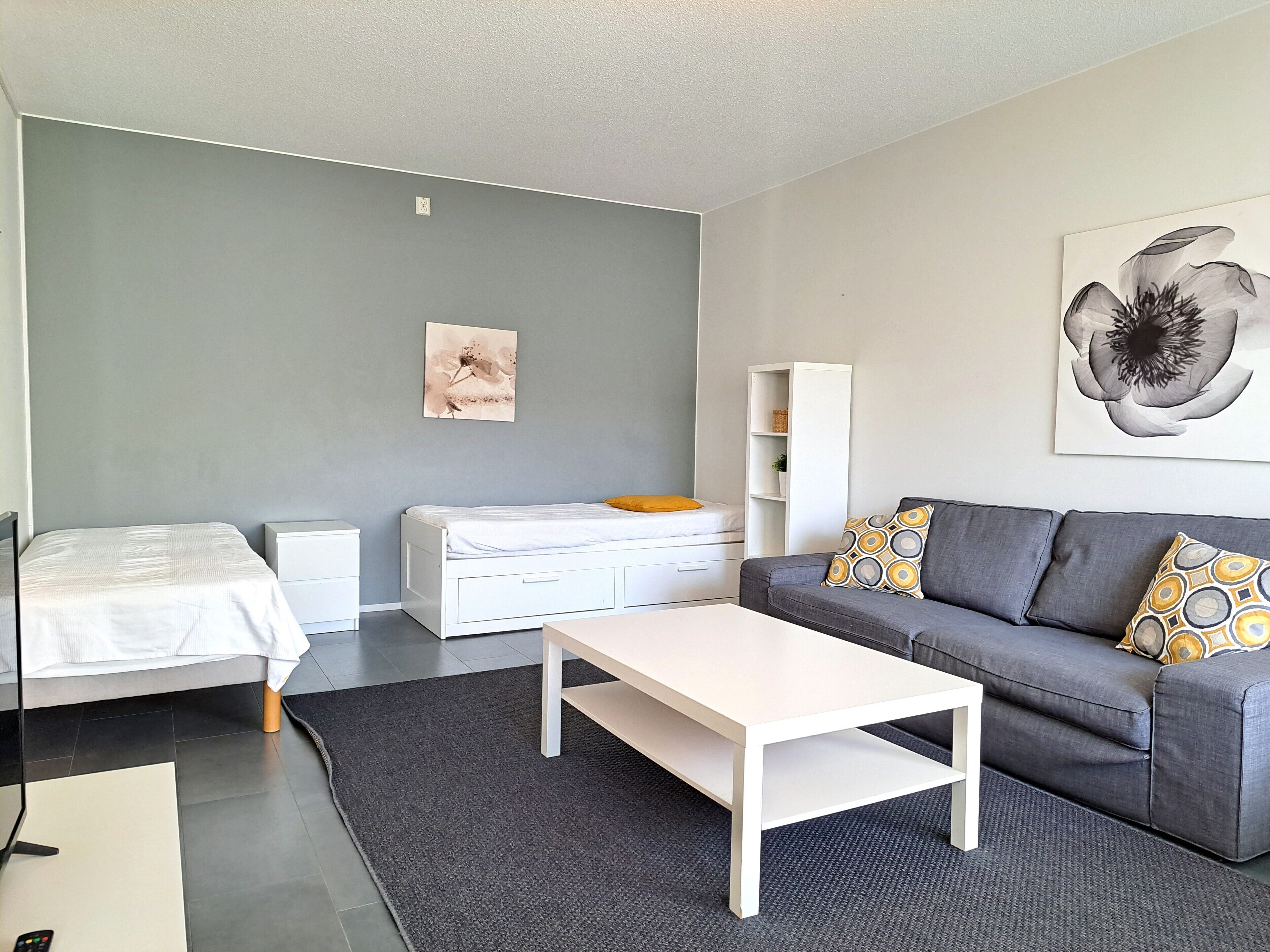 A modern living room with a grey sofa, a white coffee table, a grey carpet, a white bed, and a grey wall.