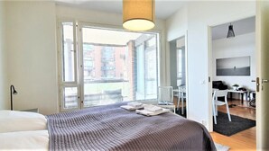 Une chambre moderne avec un grand lit, un bureau et une chaise, une grande fenêtre avec des stores et un luminaire suspendu.