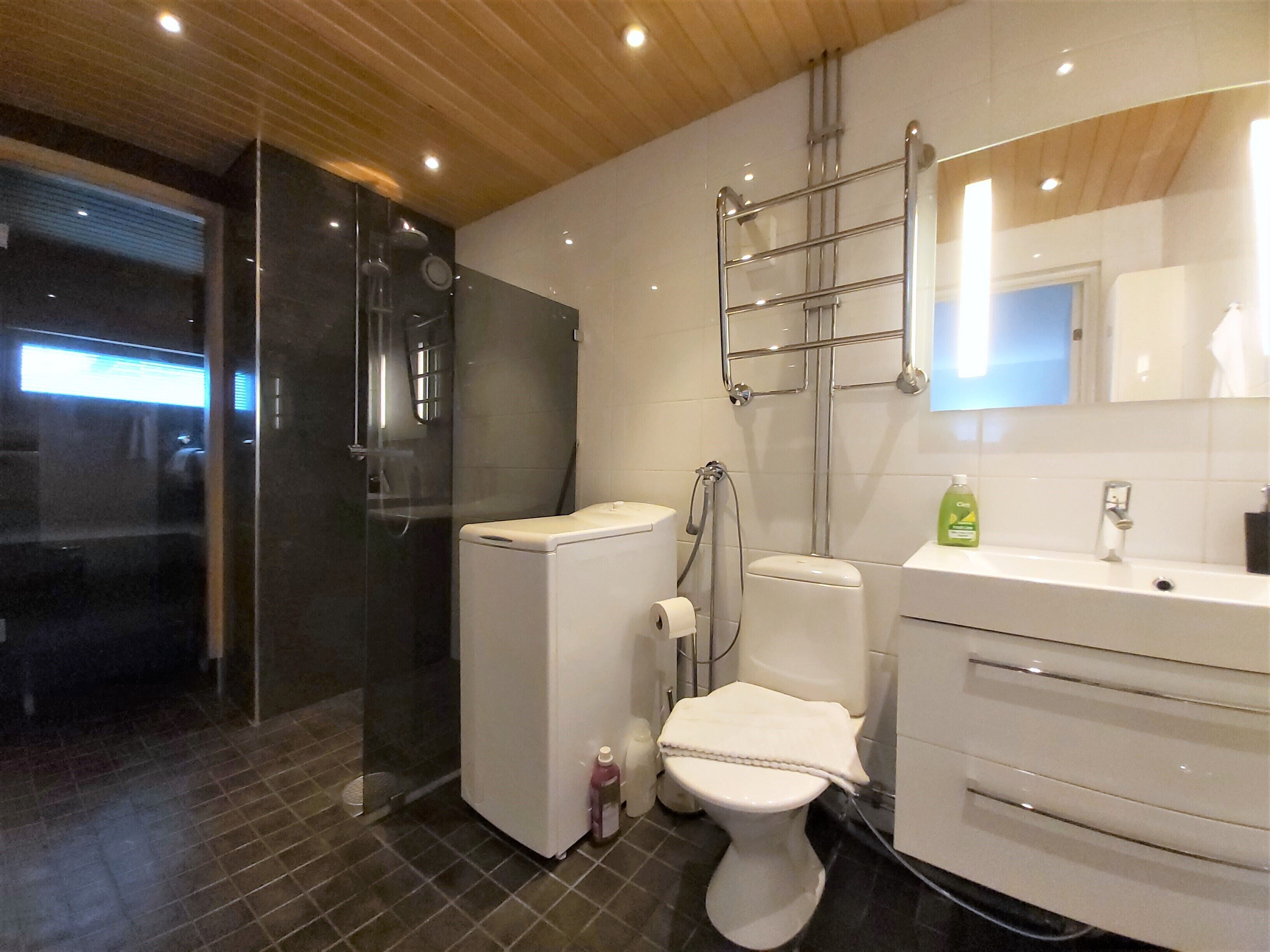 Ein modernes Badezimmer mit Duschkabine aus Glas, Toilette und Waschbecken mit Spiegel darüber.