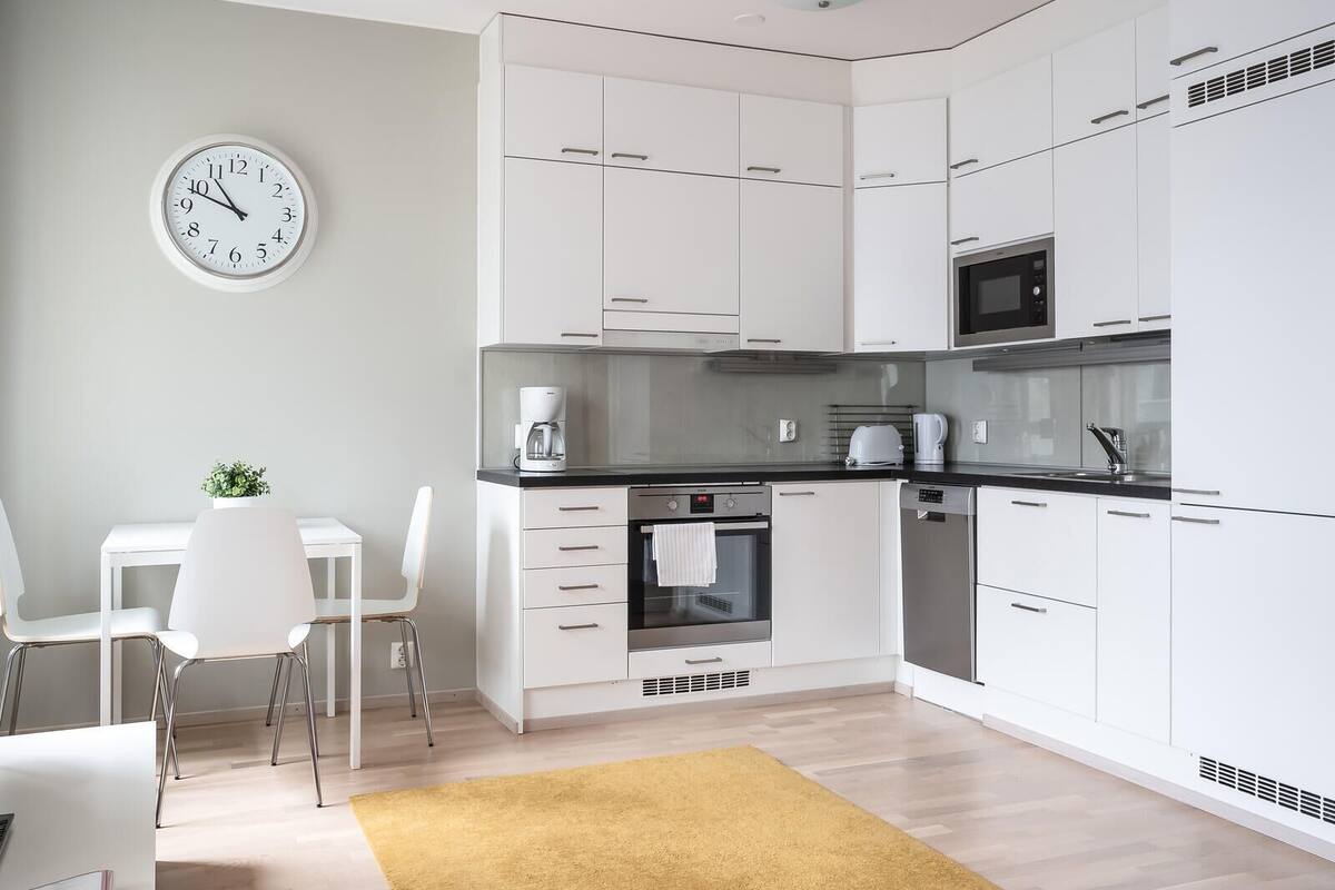 Une cuisine moderne avec des armoires blanches, un comptoir noir et un four à micro-ondes. Il y a une horloge au mur et une petite plante sur le comptoir.