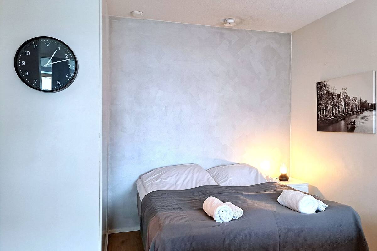 Une chambre à coucher avec un lit, une horloge et un tableau représentant un paysage urbain accroché au mur.